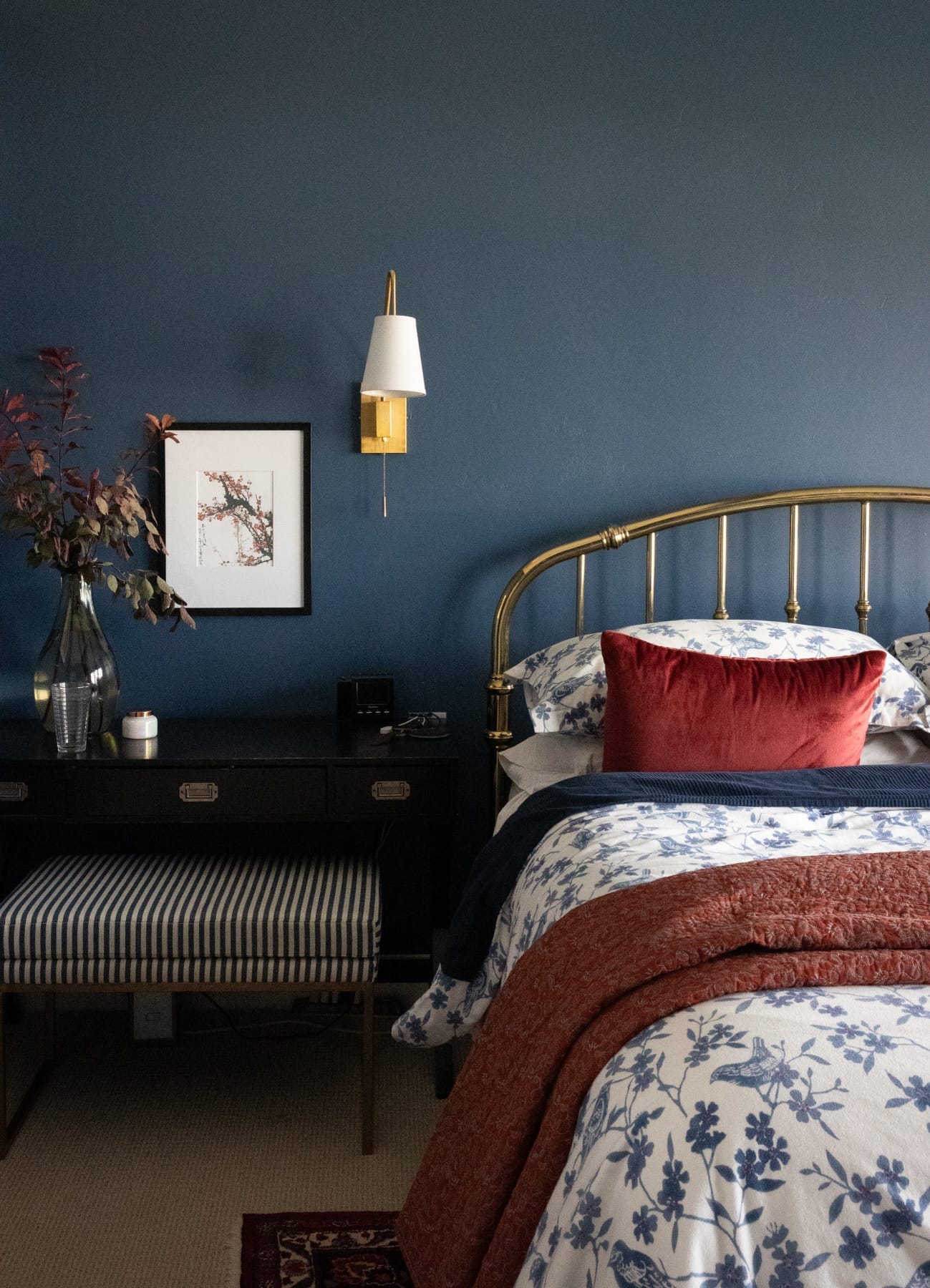 Bedside detail with a brass sconce, black nightstand and striped bench