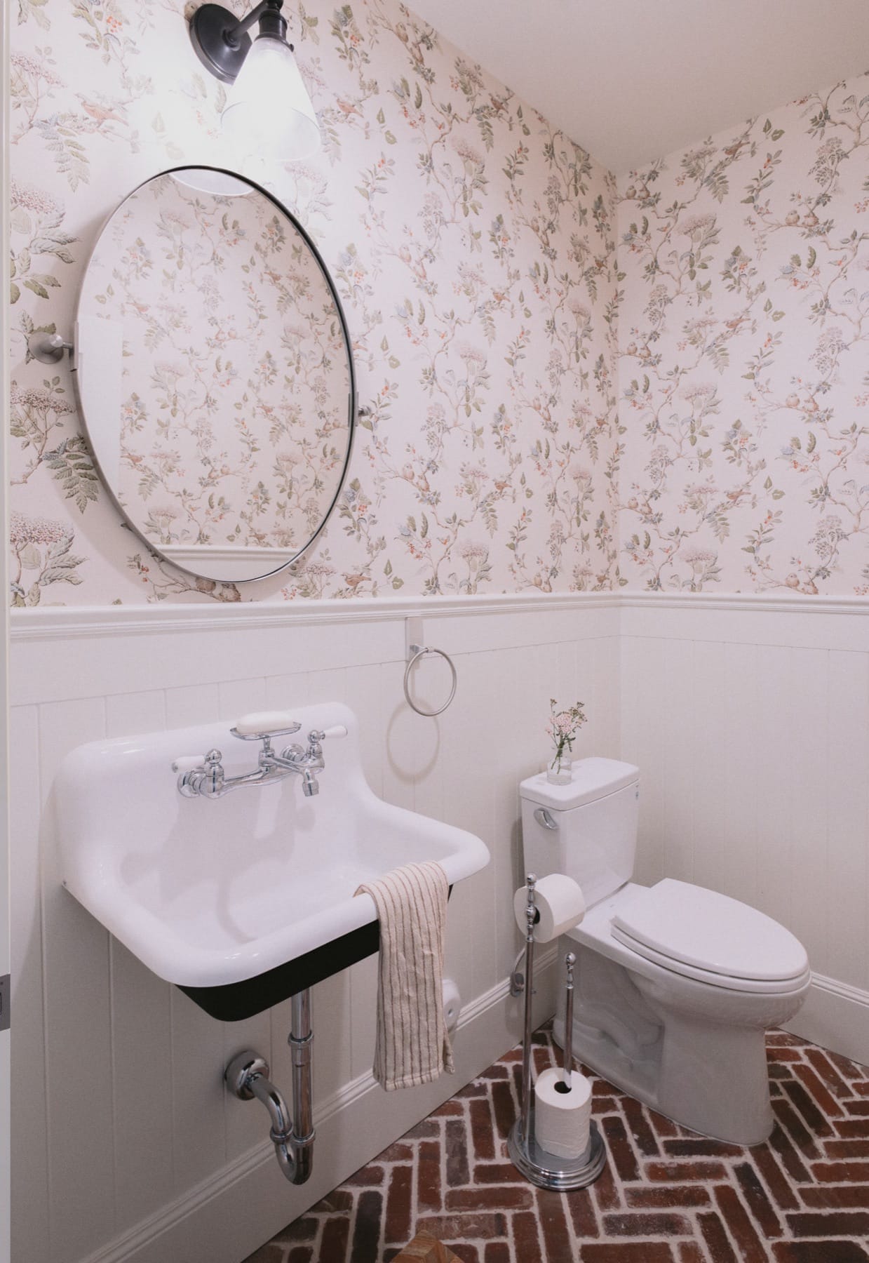 Powder room with floral wallpaper, a round mirror and a wall-mount sink