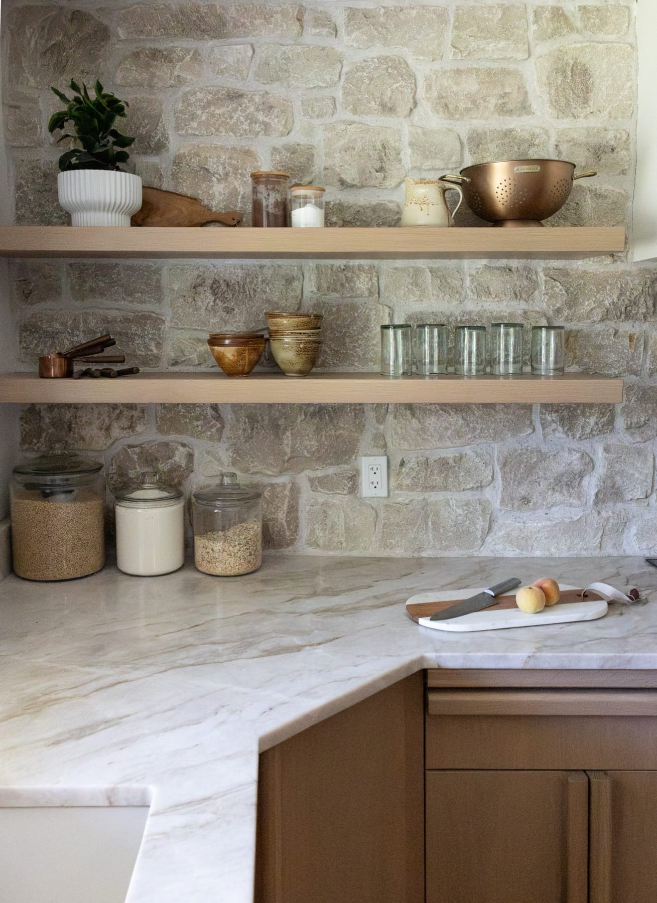 Open wood shelving on a stone wall above a marble countertop