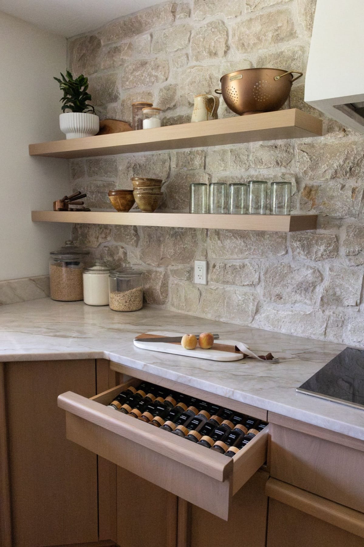 Open shelving with a copper colander and pantry jars against a stone backsplash